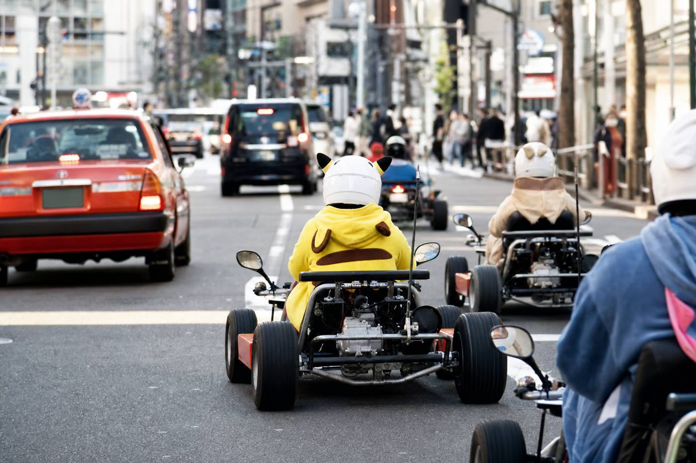 A go-kart convoy on a bright Tokyo avenue in afternoon sun