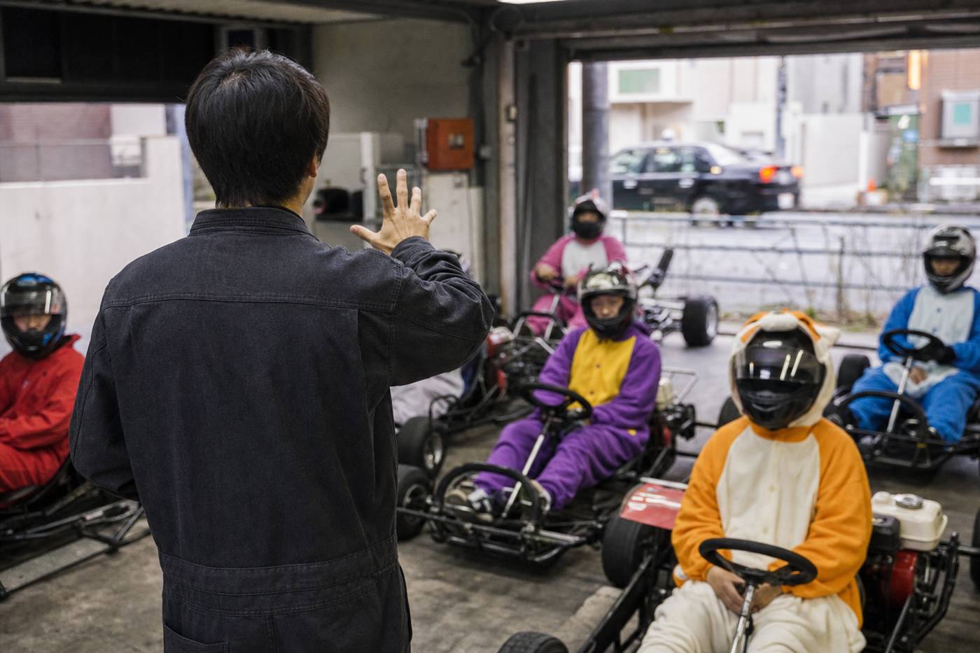 Staff briefing seated go-kart drivers in a Tokyo garage
