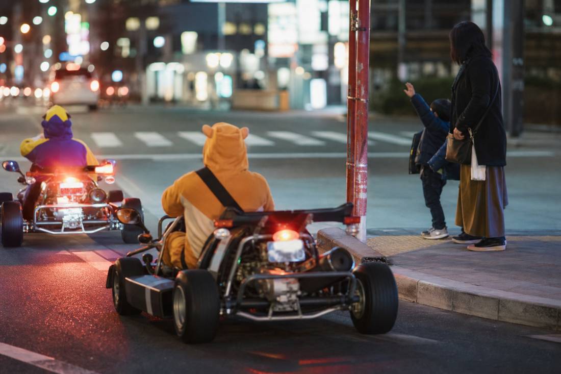 Parents on go-karts waving to a child on the sidewalk in Tokyo