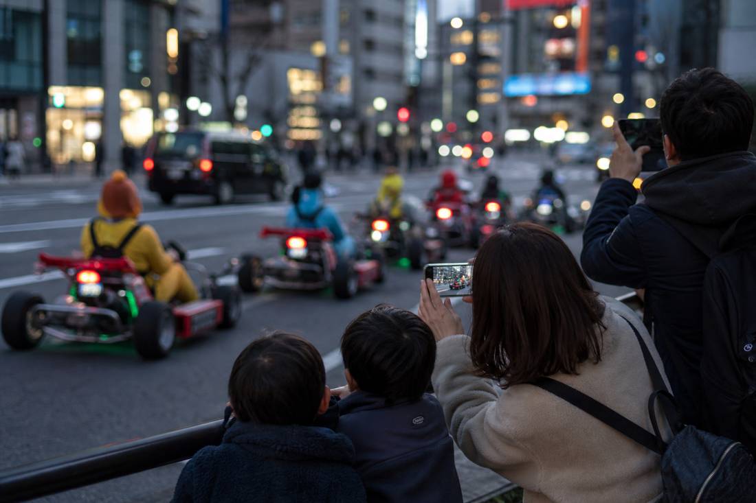 A family photographing go-karts on a neon Tokyo street