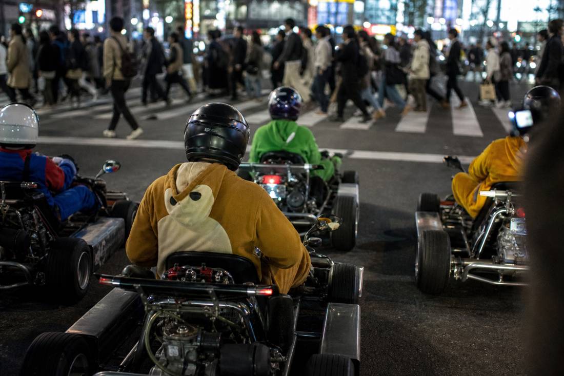 Go-karts waiting at a red light as pedestrians cross Shibuya Crossing