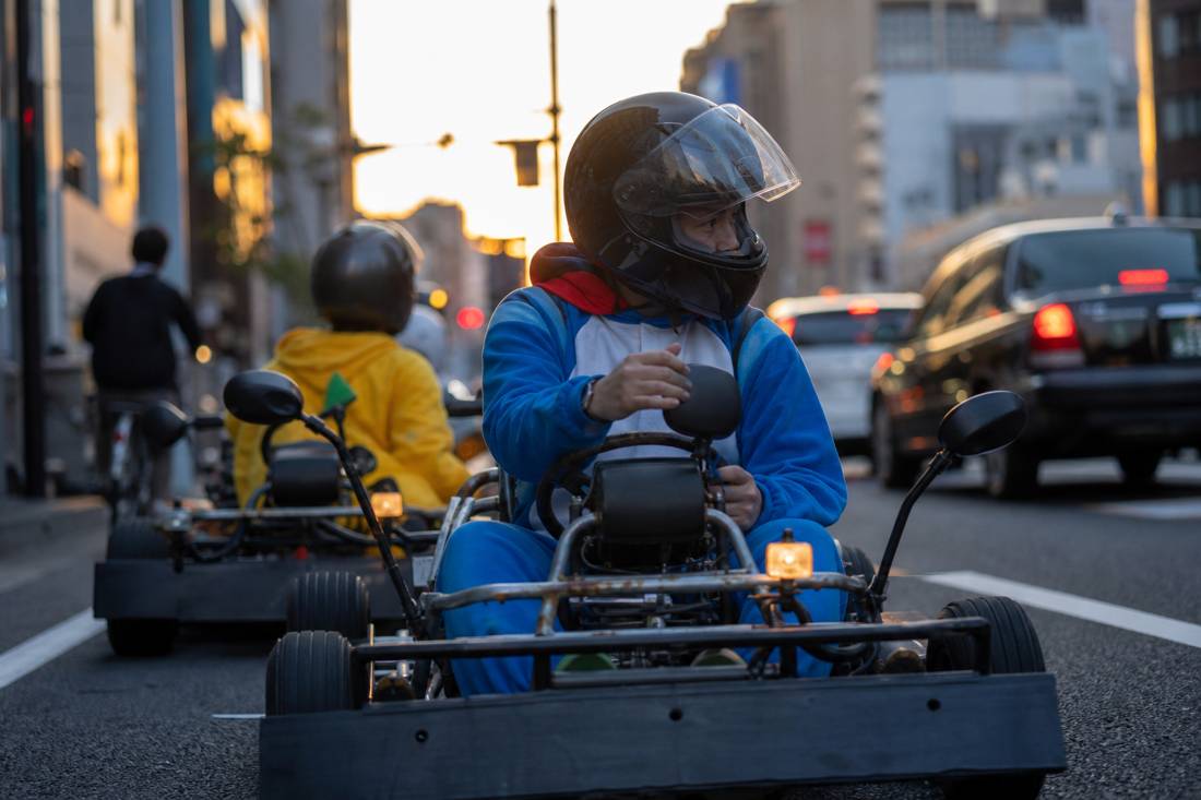 Helmeted go-kart driver checking mirrors in Tokyo traffic