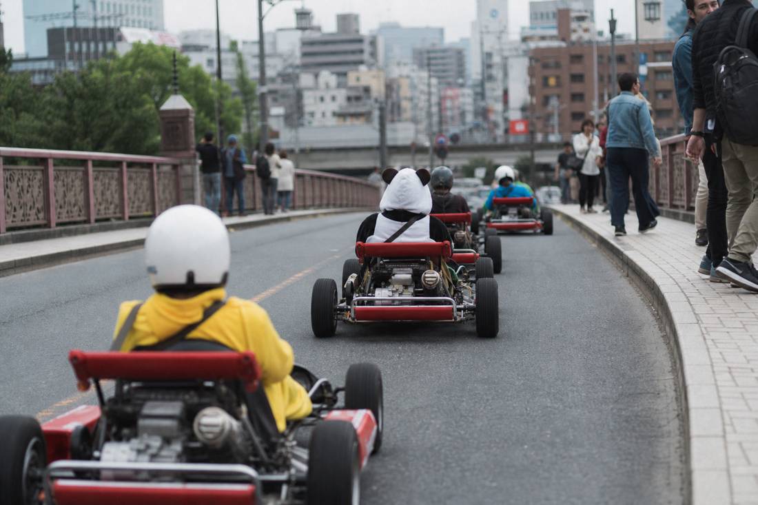 A slow go-kart convoy crossing a Tokyo bridge