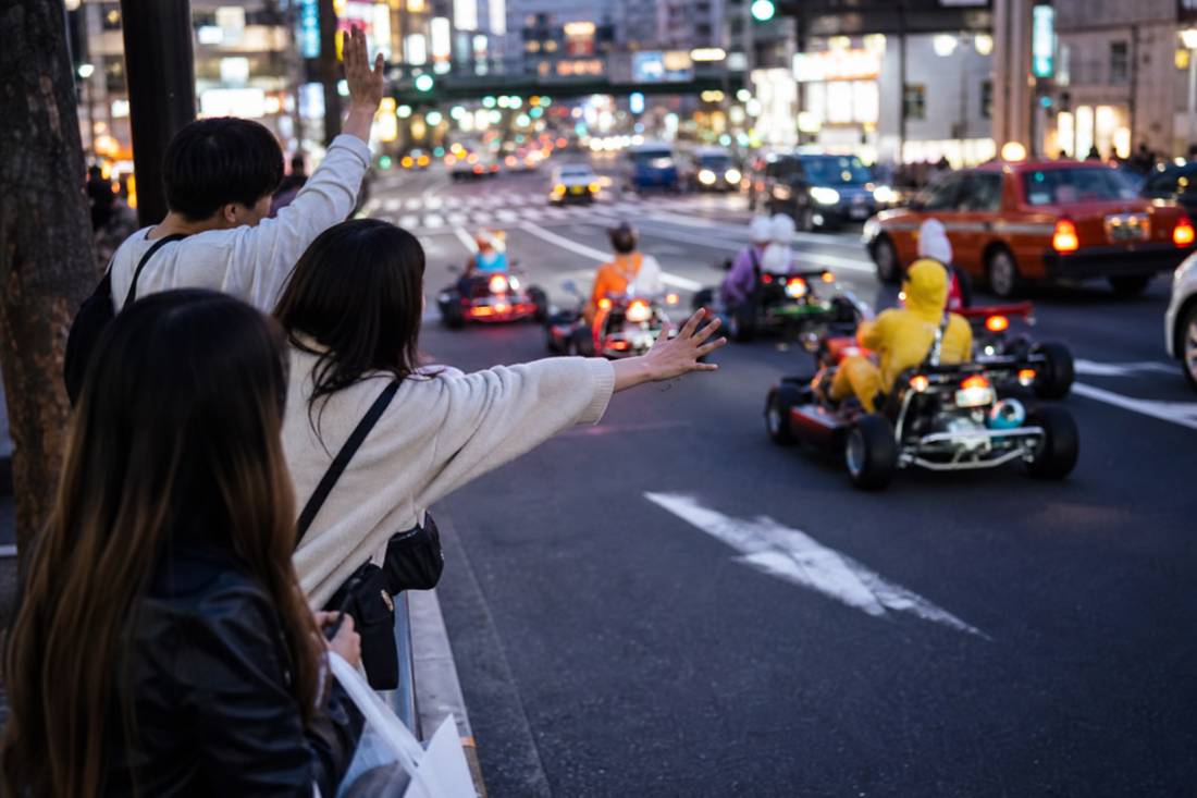 Pedestrians waving at passing go-karts in Shibuya