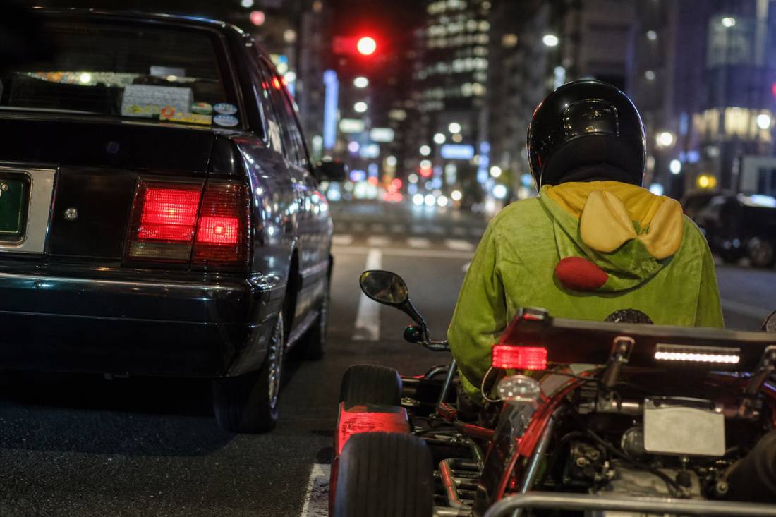 A go-kart at eye level beside a Tokyo taxi at a red light