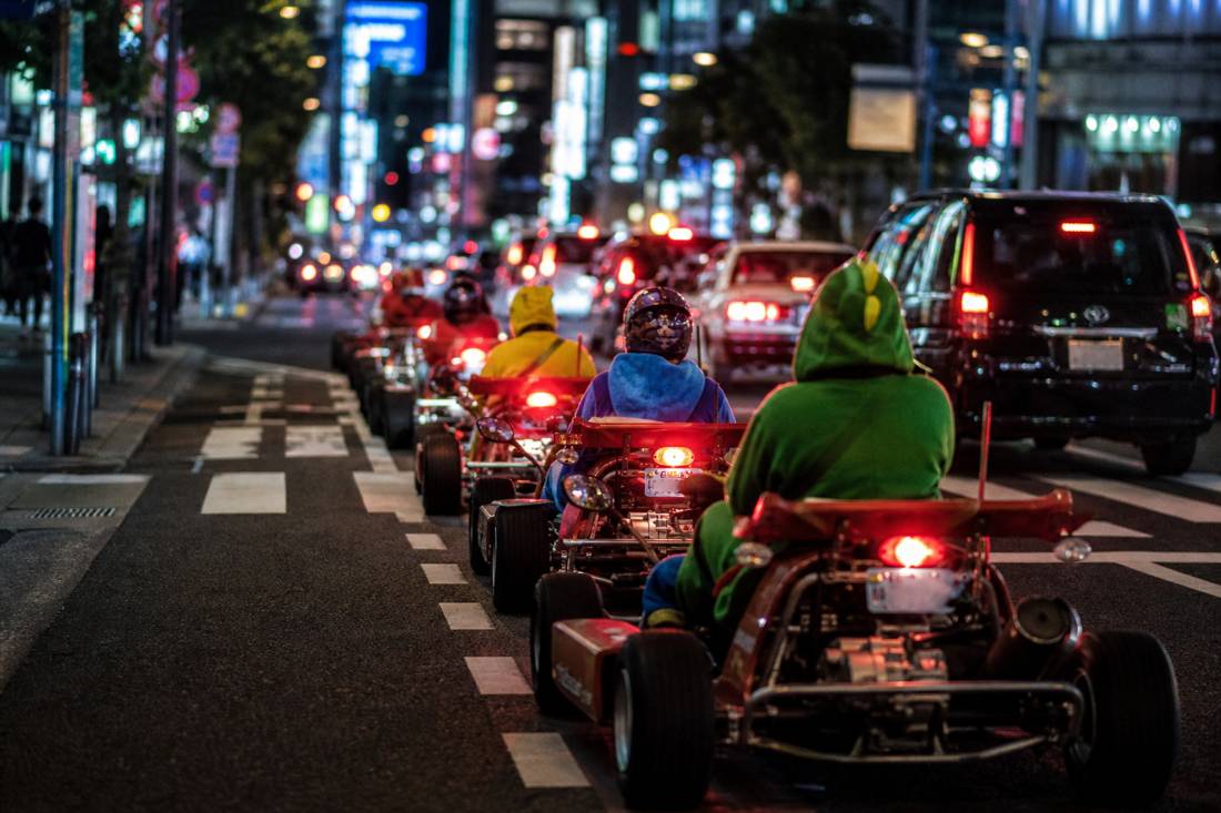 Kart convoy tail-lights in a neon Tokyo canyon at night