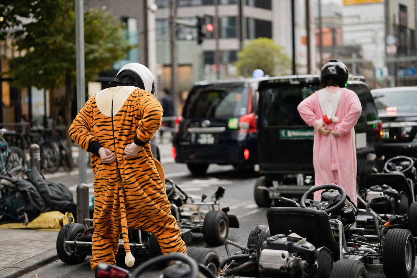 Drivers zipping colorful onesies over street clothes beside Tokyo go-karts